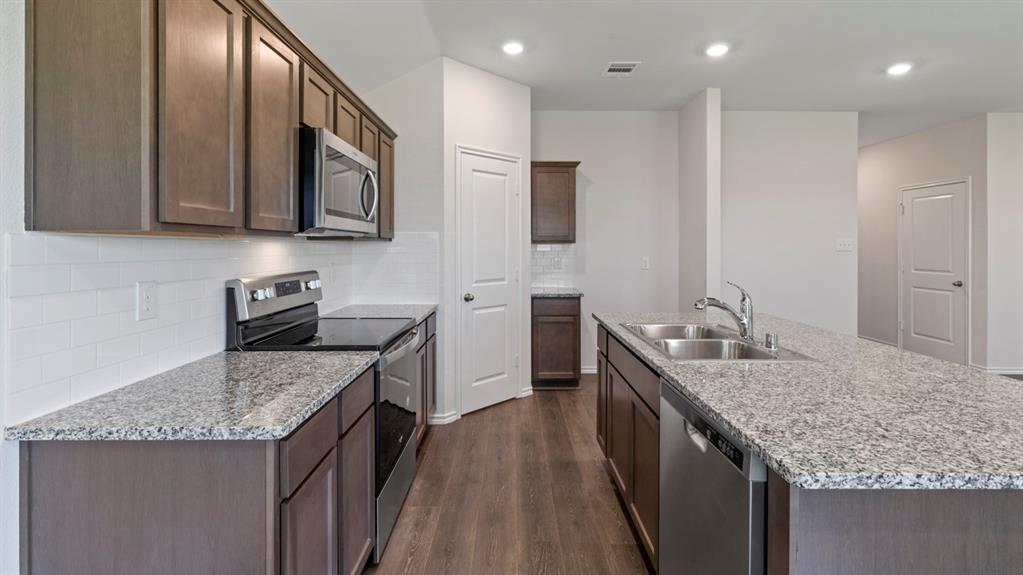 Kitchen featuring granite countertops, wood-finish flooring, stainless steel appliances, dark wood-finish cabinetry, and recessed lighting