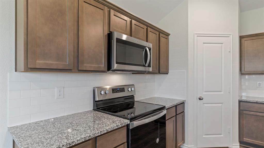 Stainless steel appliances with an electric range and built-in microwave, granite countertops, and subway tile backsplash