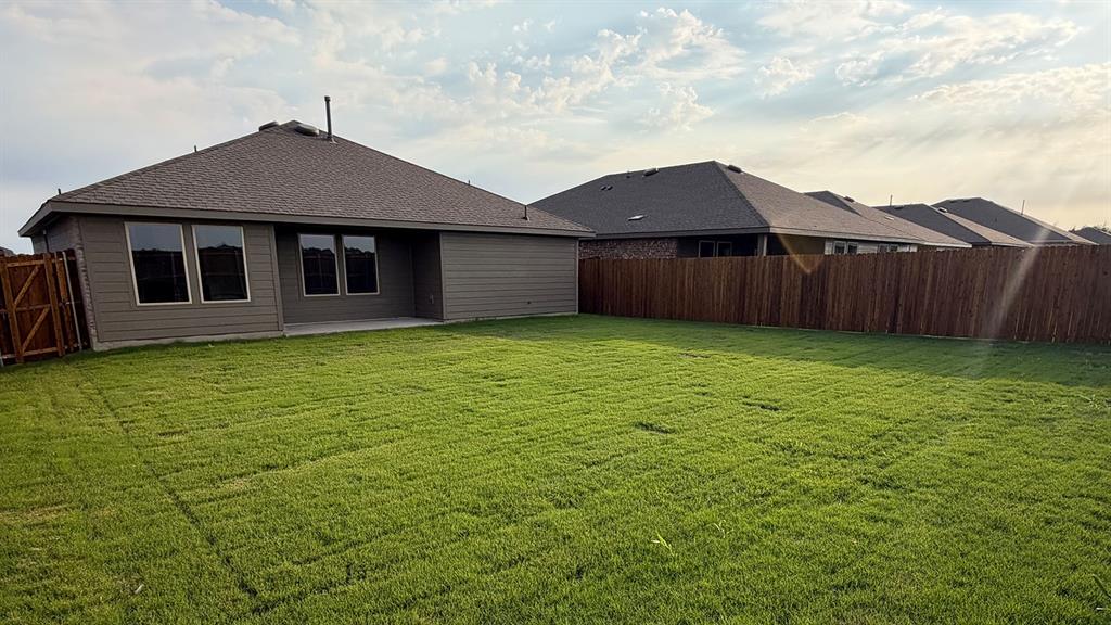 Expansive green lawn with a privacy fence, concrete patio, and dark-framed windows