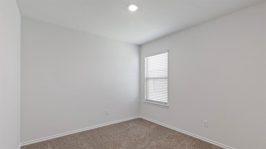 Bright, light-filled bedroom featuring neutral wall finishes, recessed ceiling lighting, carpet flooring, and a large window with plantation shutters providing natural illumination