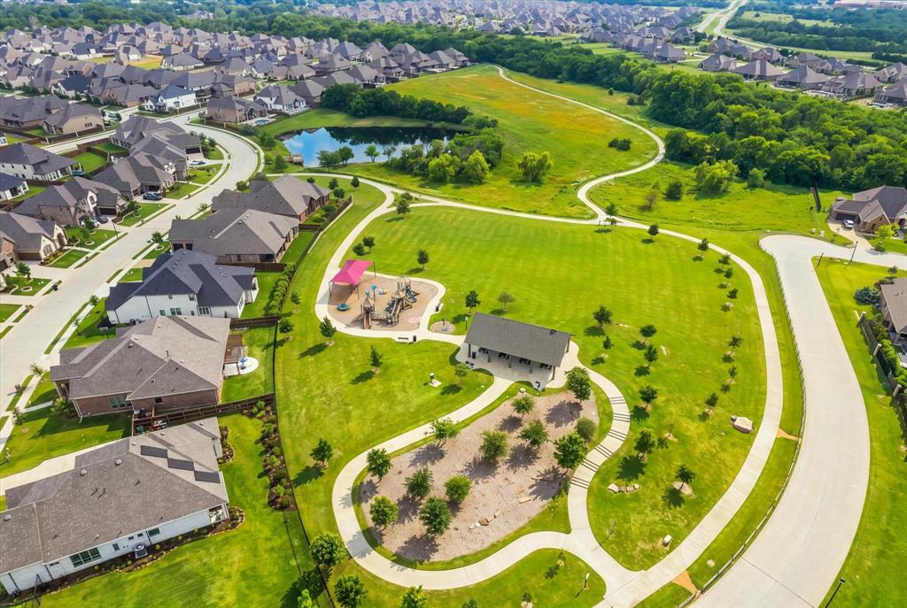 Expansive community green space featuring paved walking paths, a dedicated playground area, a central pond, and a covered pavilion