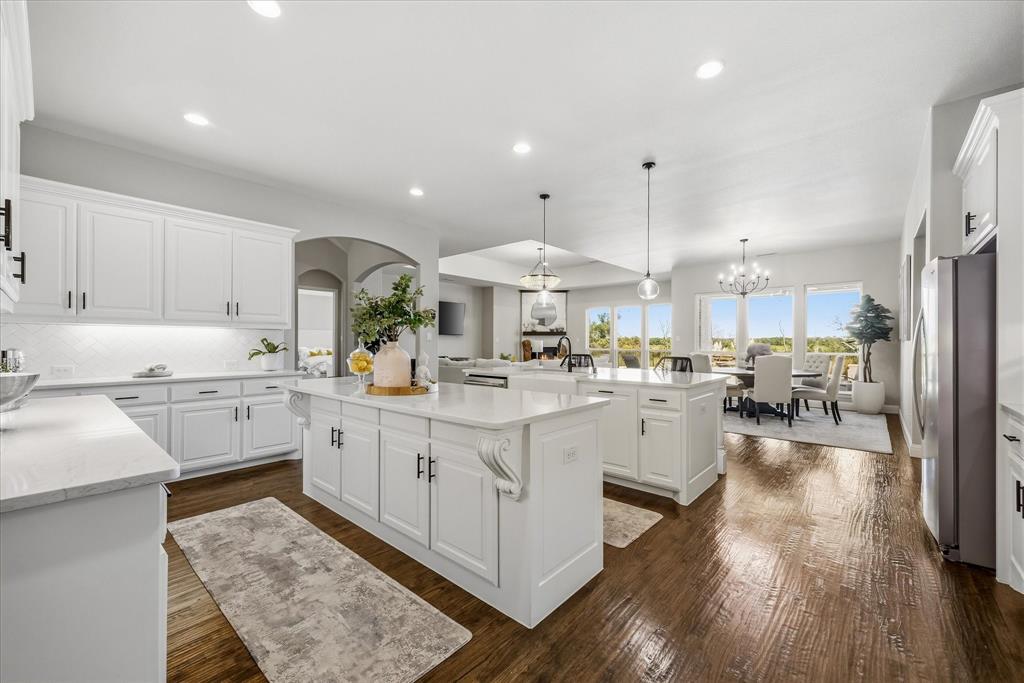 Spacious kitchen with dual islands, white cabinetry, integrated stainless steel appliances, and wood-finish flooring
