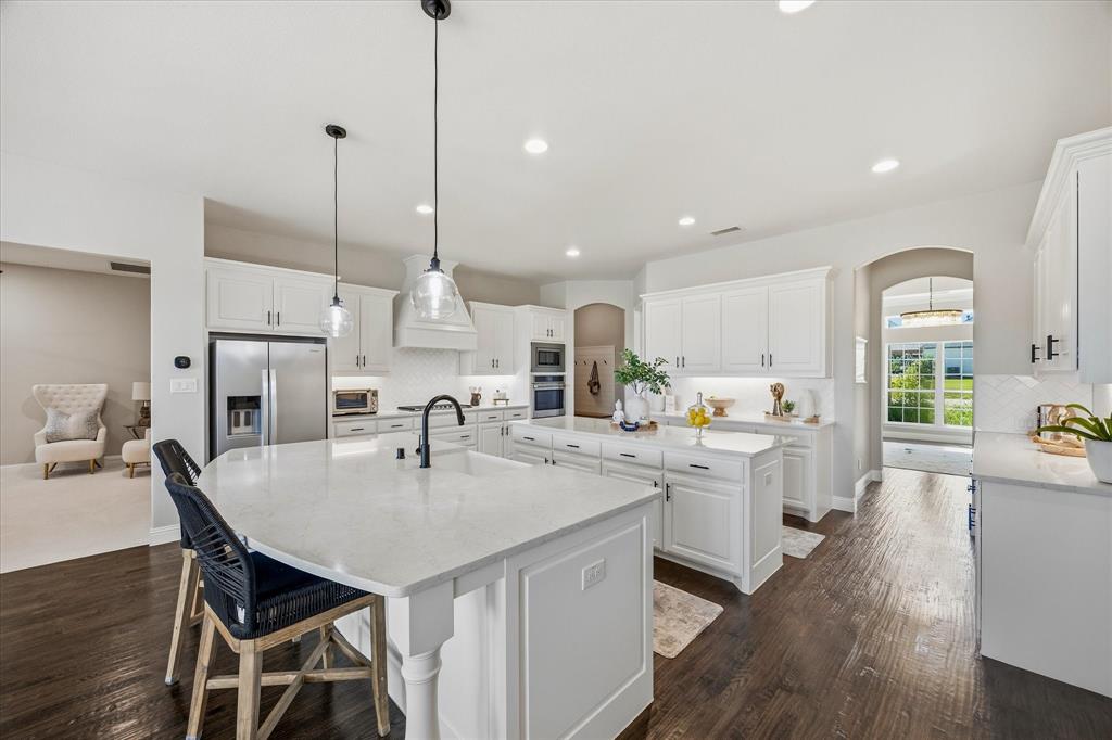 Kitchen featuring dark wood-finish flooring, white cabinetry, integrated stainless steel appliances, and two islands with light-colored countertops