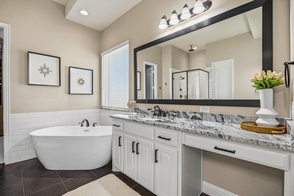 Freestanding soaking tub with dark bronze fixtures, white subway tile surround, double vanity with granite countertop, dark bronze hardware, and a large framed mirror
