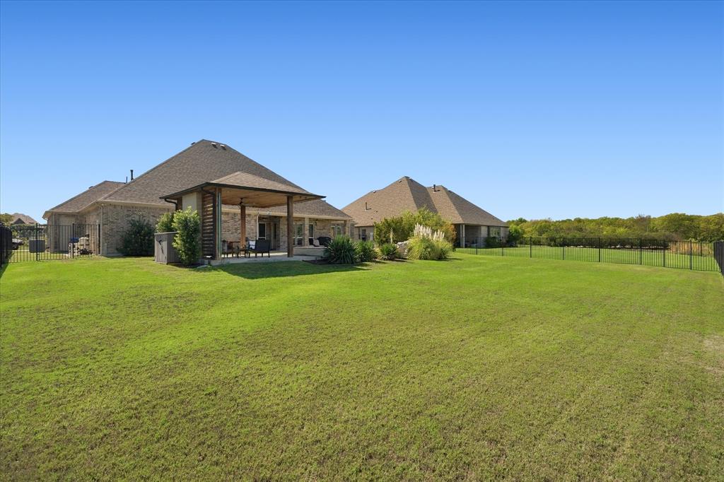 Expansive rear lawn featuring a covered patio, brick exterior, and dark-finish perimeter fencing