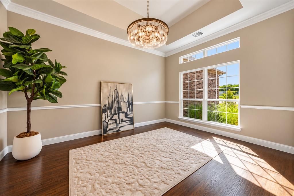 Tray ceiling, drum-style crystal chandelier, wood-finish flooring, and crown molding complemented by chair rail trim