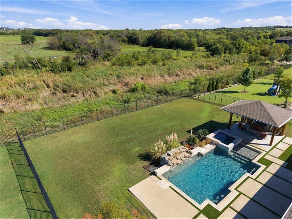 Private backyard featuring a swimming pool with integrated spa, a stone-clad waterfall, a covered outdoor living area, and expansive lawn space