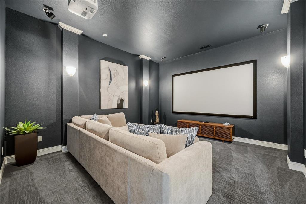 Dedicated media room featuring a large projection screen, mounted projector, recessed lighting, wall sconces, and a dark carpeted floor
