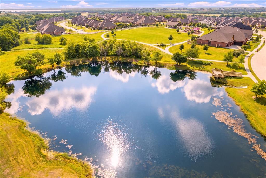 Residential community featuring a prominent pond with a wooden dock, surrounded by green spaces and paved pathways