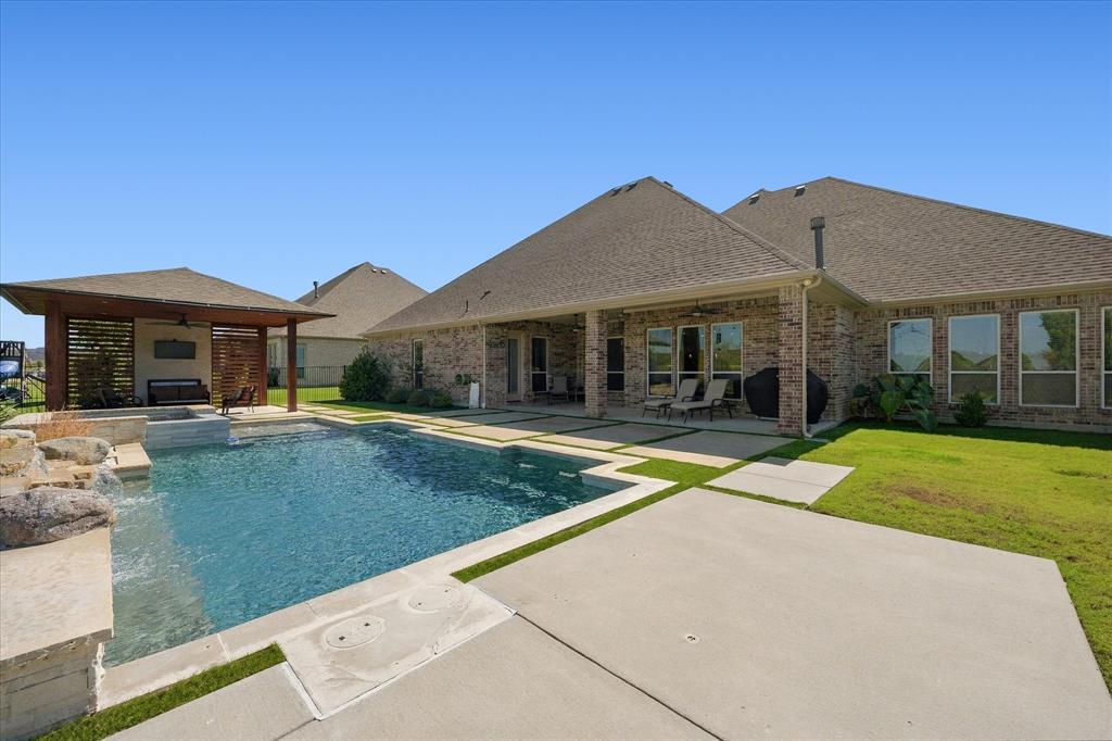 Expansive backyard featuring a rectangular swimming pool with a stone waterfall, a covered patio, and a separate covered outdoor structure