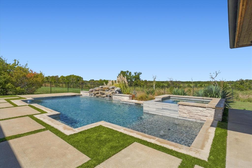 Expansive outdoor area featuring a swimming pool, integrated spa, rock waterfall, and large format concrete pavers with artificial turf accents