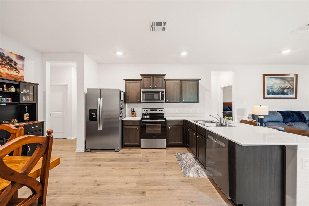 Modern kitchen featuring wood-finish flooring, stainless steel appliances, dark wood-finish cabinetry, a white subway tile backsplash, and a white countertop