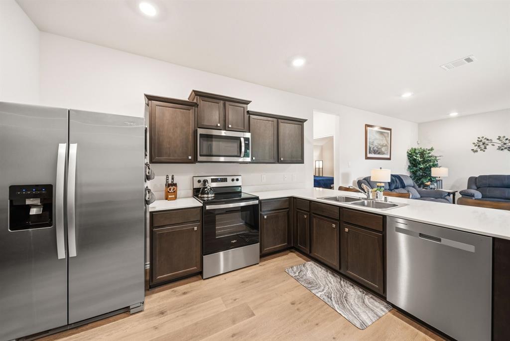Kitchen featuring wood-finish flooring, dark wood cabinetry, stainless steel appliances, and solid surface countertops