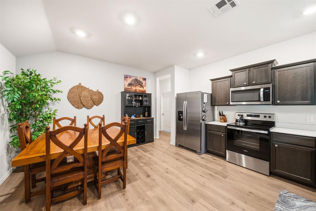 Open-concept living space with wood-finish flooring, recessed lighting, and a kitchen featuring stainless steel appliances, dark wood-finish cabinetry, and solid surface countertops
