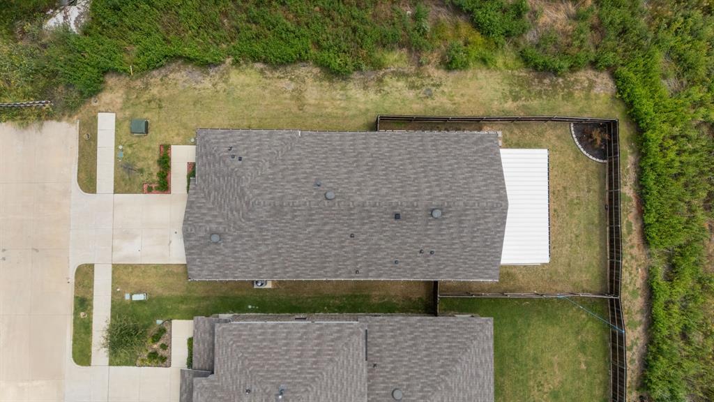Gabled roofline with asphalt shingles, concrete driveway, concrete walkways, wood fencing, and a white metal roof structure