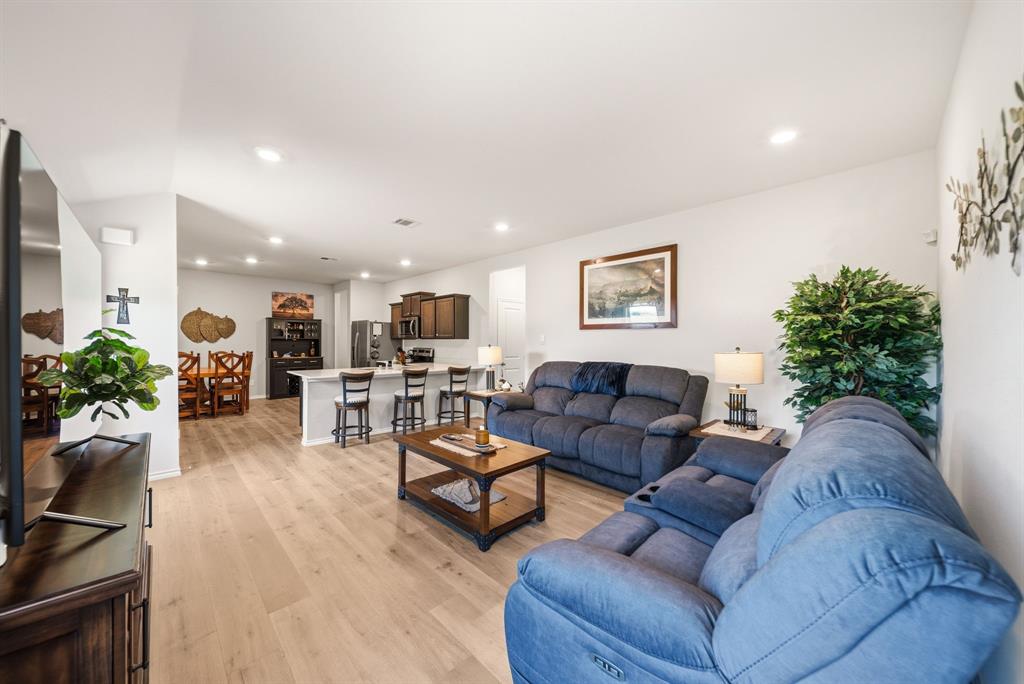 Open-concept living area featuring light wood-finish flooring, recessed lighting, and a kitchen with an island and breakfast bar