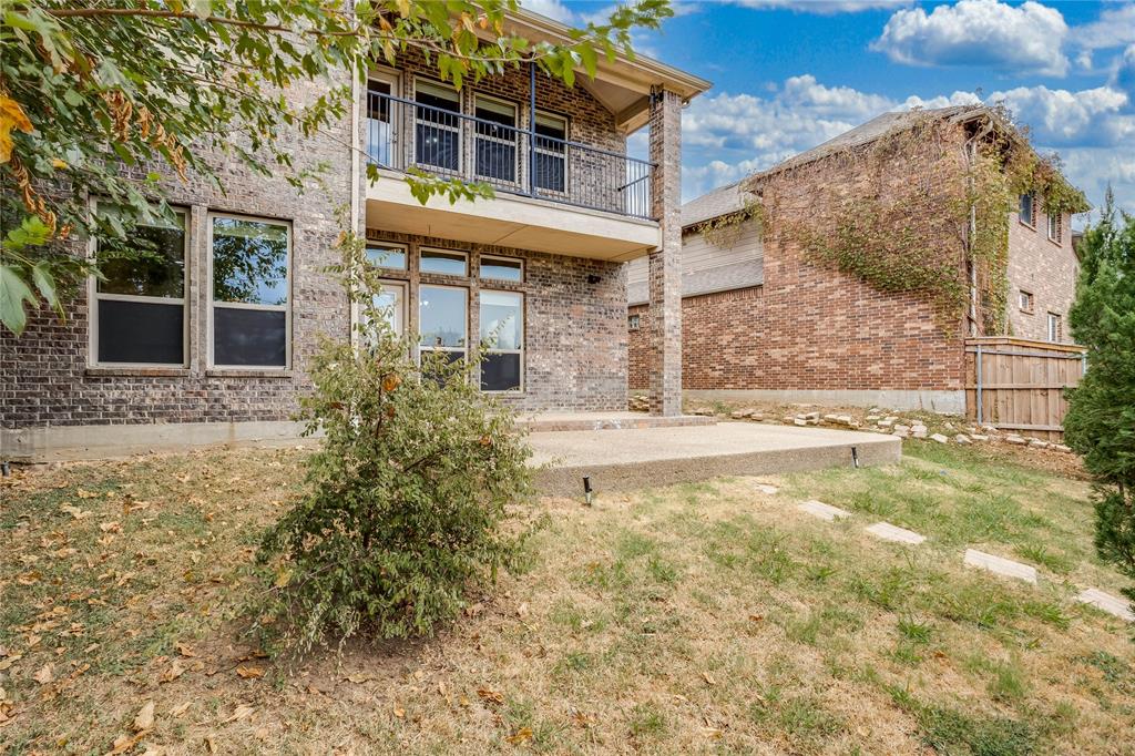 Brick exterior featuring multiple windows, an upper-level balcony with metal railing, and a ground-level concrete patio