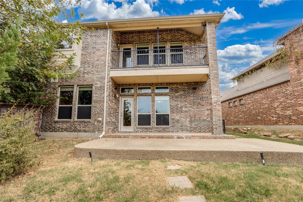 Brick exterior with multiple windows, a second-story balcony with metal railing, and a ground-level concrete patio