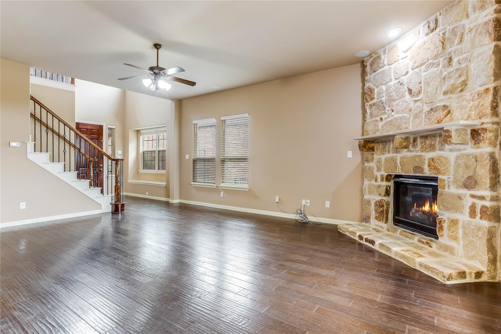 Stone-clad fireplace with hearth, dark wood-finish flooring, staircase with dark wood handrail and iron balusters, recessed lighting, and ceiling fan with integrated lighting