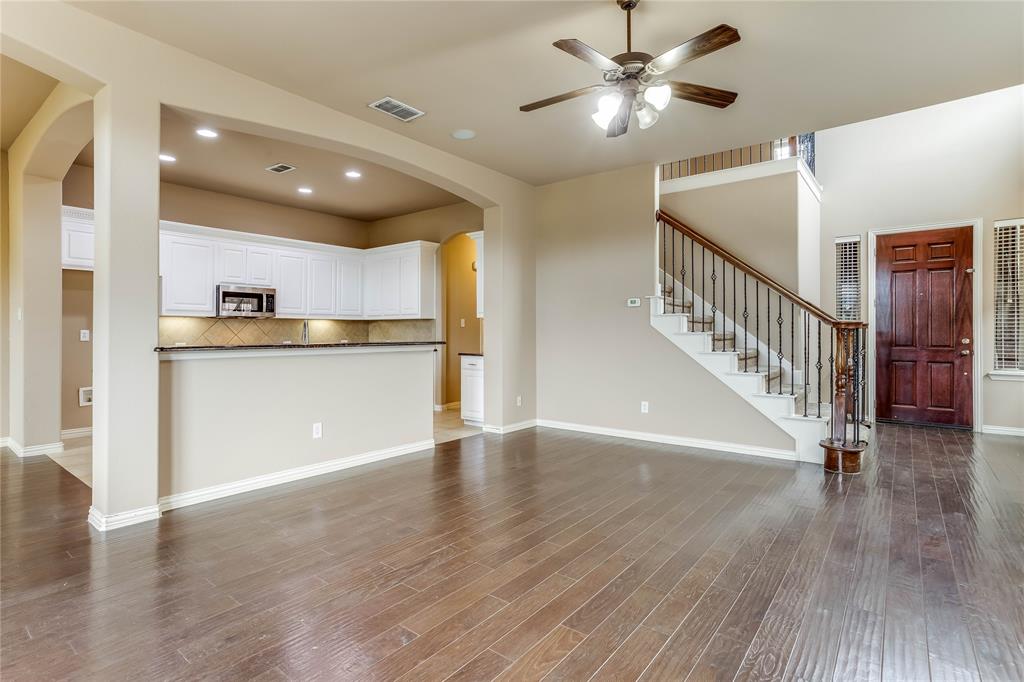 Hardwood flooring, two-story ceiling, dark wood-paneled door, recessed lighting, and a staircase with decorative iron balusters
