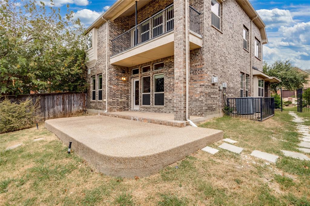 Two-story brick exterior with an upper-level balcony featuring wrought iron railing, a ground-level concrete patio, and a fenced yard with stepping stones