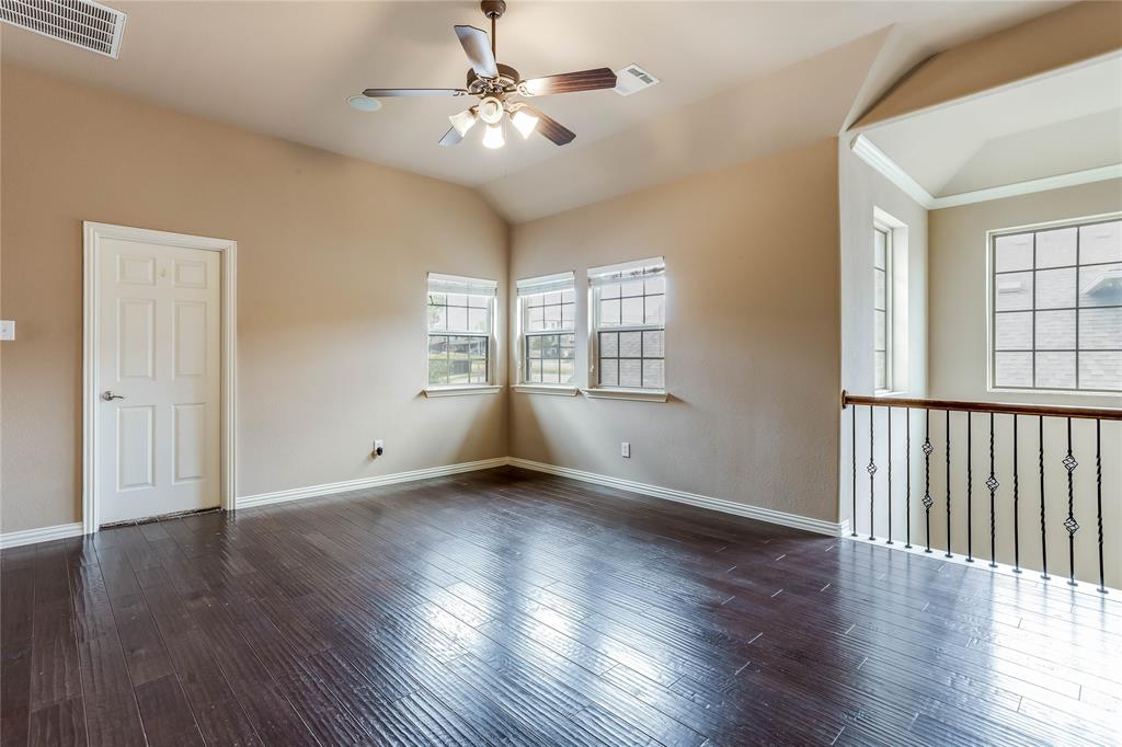 Vaulted ceiling with a ceiling fan, three windows, wood-finish flooring, and an open railing with decorative metal spindles