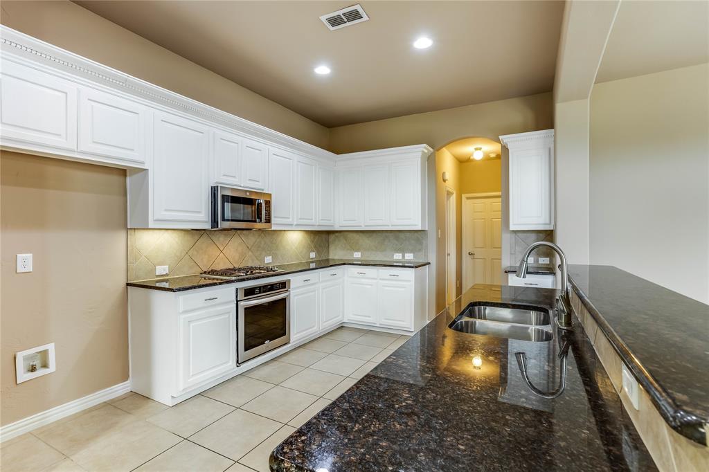 Kitchen featuring white cabinetry, dark stone countertops, stainless steel appliances, and a tile backsplash