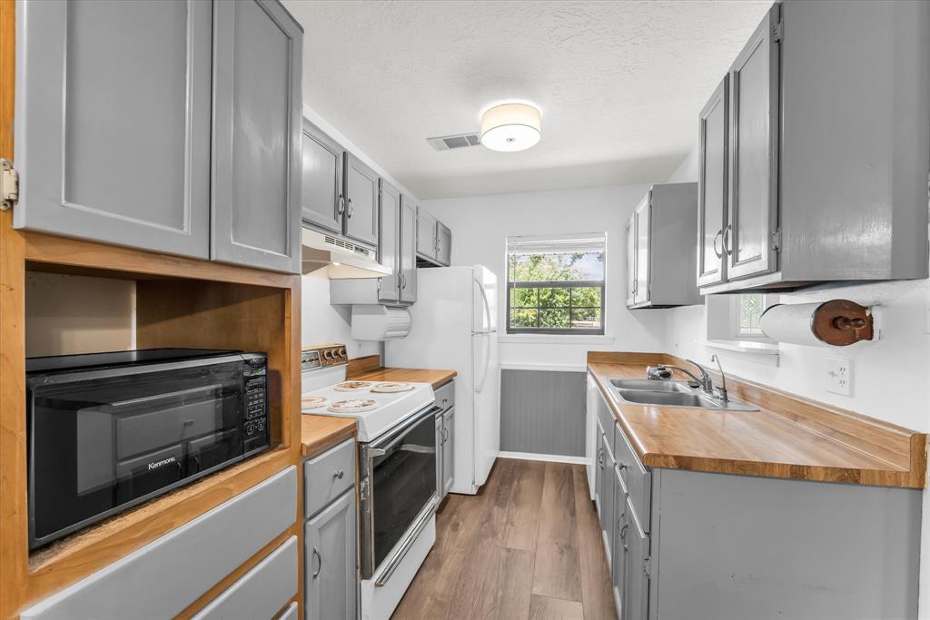 Kitchen featuring wood-finish flooring, light gray cabinetry, wood countertops, and a double basin sink