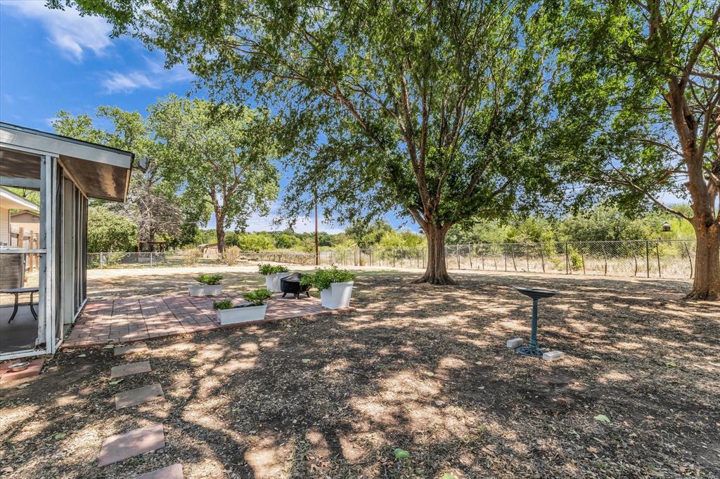 Expansive outdoor area featuring a screened-in porch, brick paver patio, and mature trees providing natural shade