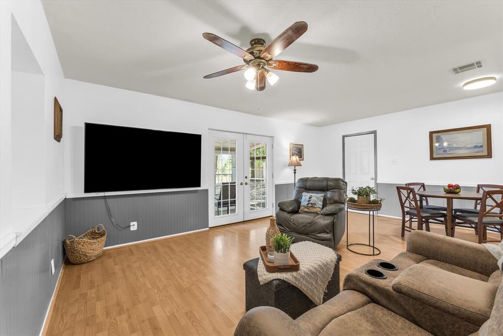 Spacious living area featuring wood-finish flooring, white walls with gray wainscoting, and a ceiling fan with integrated lighting