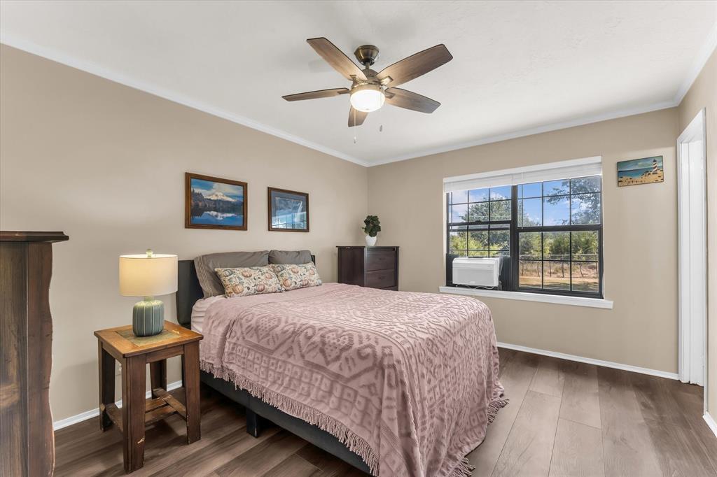 Wood-finish flooring, ceiling fan with integrated lighting, window with exterior scenery, crown molding, and neutral wall tones