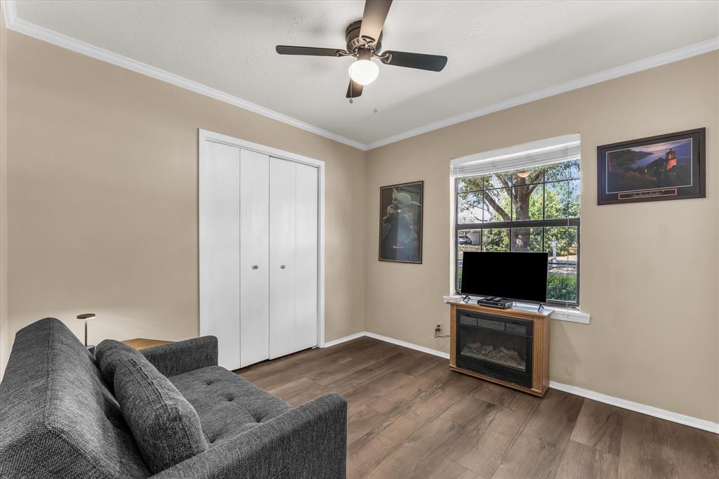 Wood-finish flooring, white bi-fold closet doors, ceiling fan with integrated lighting, white crown molding, and a window with exterior tree scenery
