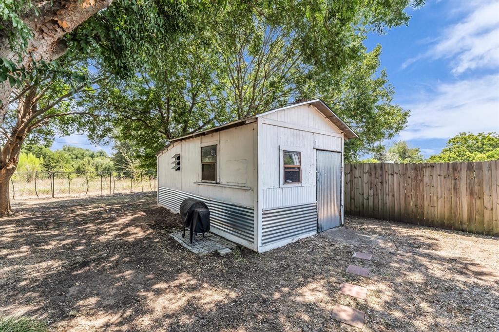 Storage shed with corrugated metal siding, wood-plank fencing, and mature trees