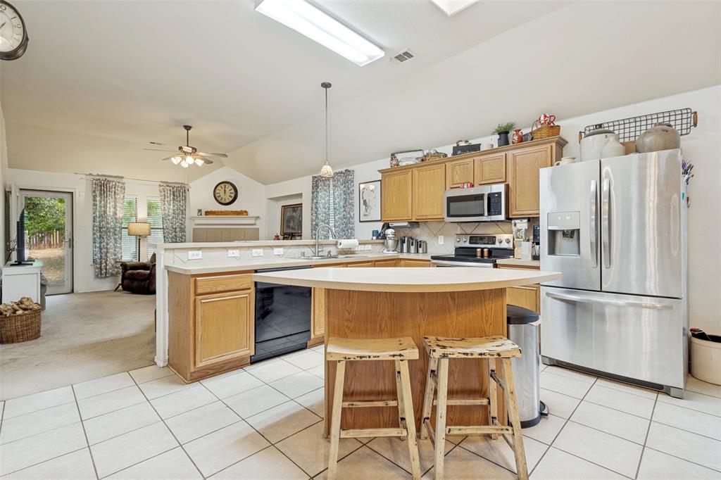 Kitchen featuring tile flooring, wood-finish cabinetry, stainless steel appliances, and a breakfast bar