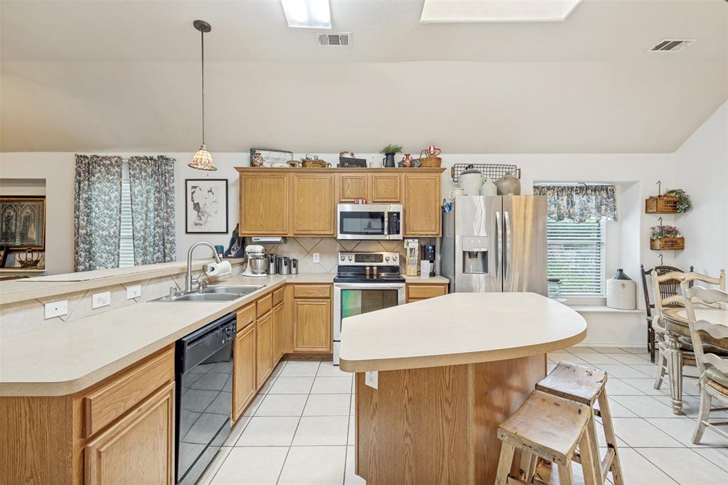 Kitchen featuring wood cabinetry, stainless steel appliances, a center island, and white tile flooring