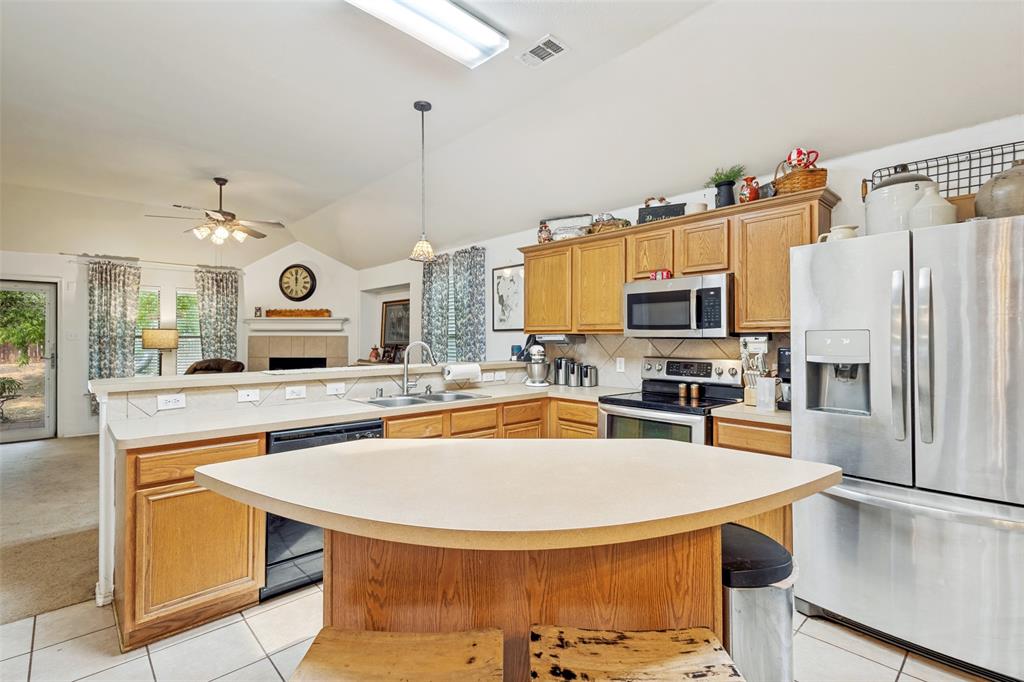 Kitchen featuring wood cabinetry, stainless steel appliances, a corner sink with a stainless steel faucet, a breakfast bar, and tile flooring