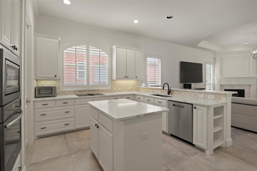 White cabinetry with dark hardware, a center island with a stone countertop, built-in double oven, integrated dishwasher, and a tile backsplash