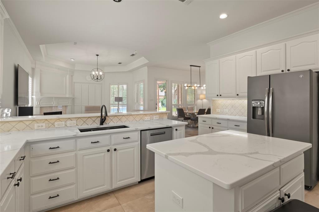 White cabinetry with black hardware, white countertops, tile backsplash, built-in stainless steel appliances, and a central island