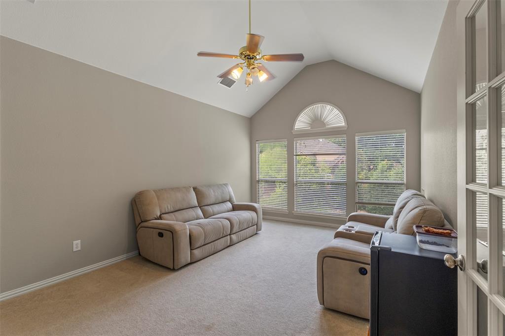 Vaulted ceiling with an illuminated ceiling fan, a series of windows, and a glass-paneled door