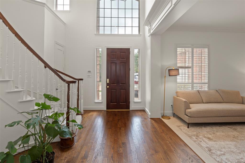 Two-story entry with hardwood flooring, a multi-pane arched window, and a grand staircase featuring a wood handrail