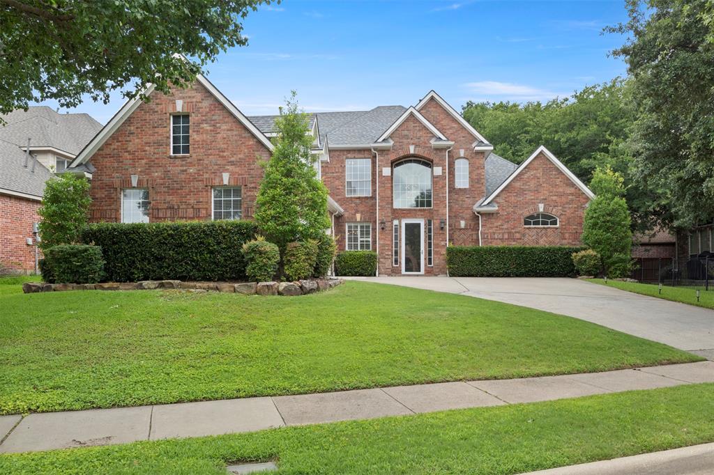 Brick exterior with a gabled roofline, arched window, mature landscaping, paved driveway, and established trees Brick exterior with a gabled roofline, arched window, mature landscaping, paved driveway, and established trees