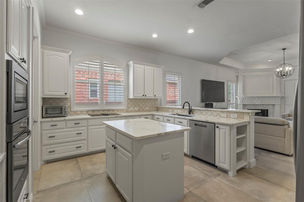 White cabinetry with black hardware, built-in double ovens, center island, stainless steel dishwasher, and recessed lighting