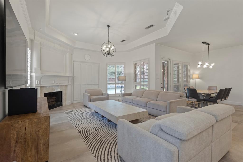 Recessed lighting, tray ceiling, fireplace with stone surround, wood-finish flooring, and plantation shutters