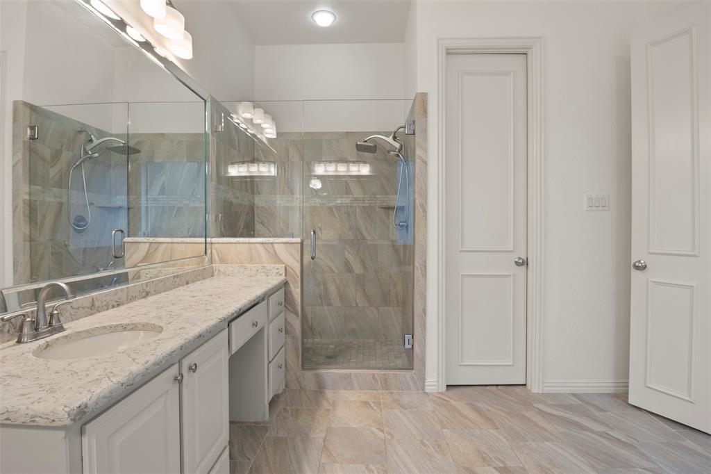 Dual vanity with light-toned countertop, glass-enclosed shower, and full-height wall tiling