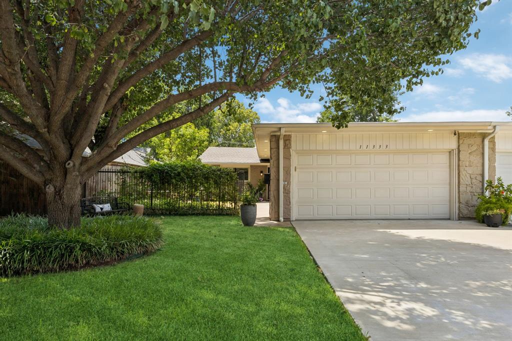Attached garage with a panel door, stone accents, and an expansive driveway