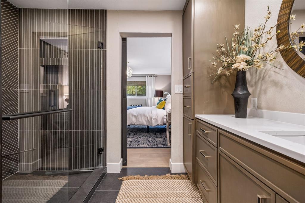Glass-enclosed shower with ribbed tile, built-in vanity with white quartz countertop, and integrated cabinetry