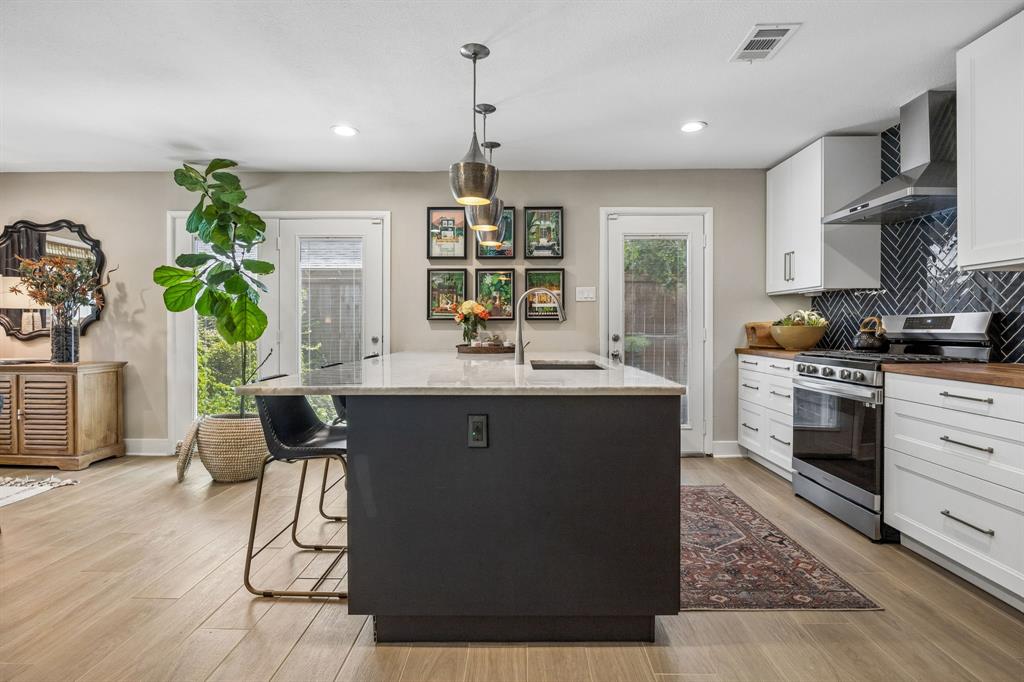 Modern kitchen featuring a spacious island with a quartzite countertop, recessed lighting, wood-finish flooring, white cabinetry, and a dark-toned herringbone tile backsplash