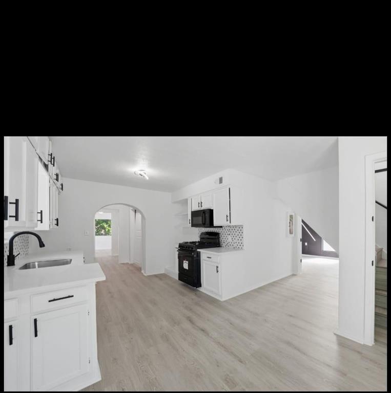 White cabinetry with matte black hardware, integrated sink with matte black faucet, light wood-finish flooring, and arched doorways
