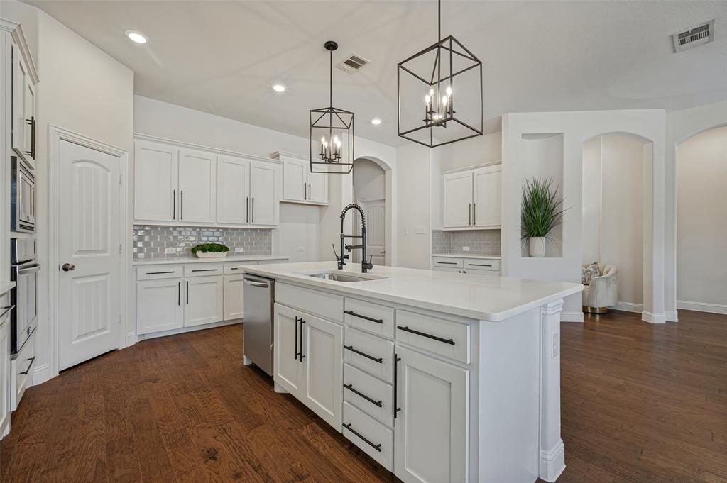 Spacious kitchen featuring white cabinetry, stainless steel appliances, a center island with a sink, and dark wood-finish flooring