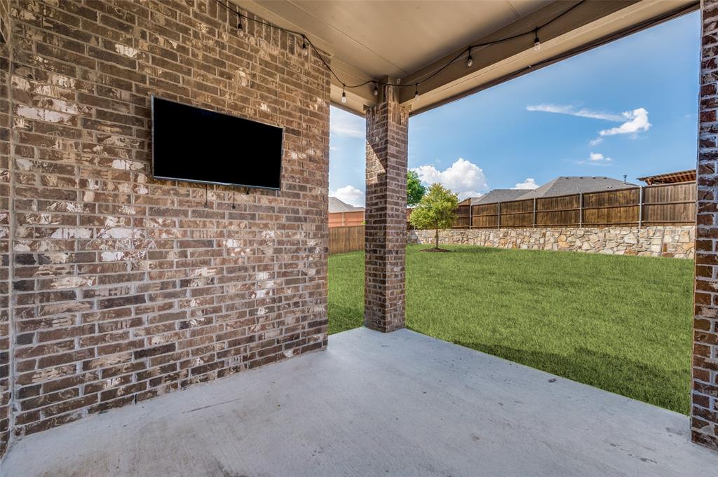 Covered patio with a brick accent wall, concrete flooring, string lighting, and a manicured lawn